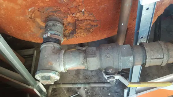 Galvanized tee and ball valve fitted below a heavily rusted steel water tank