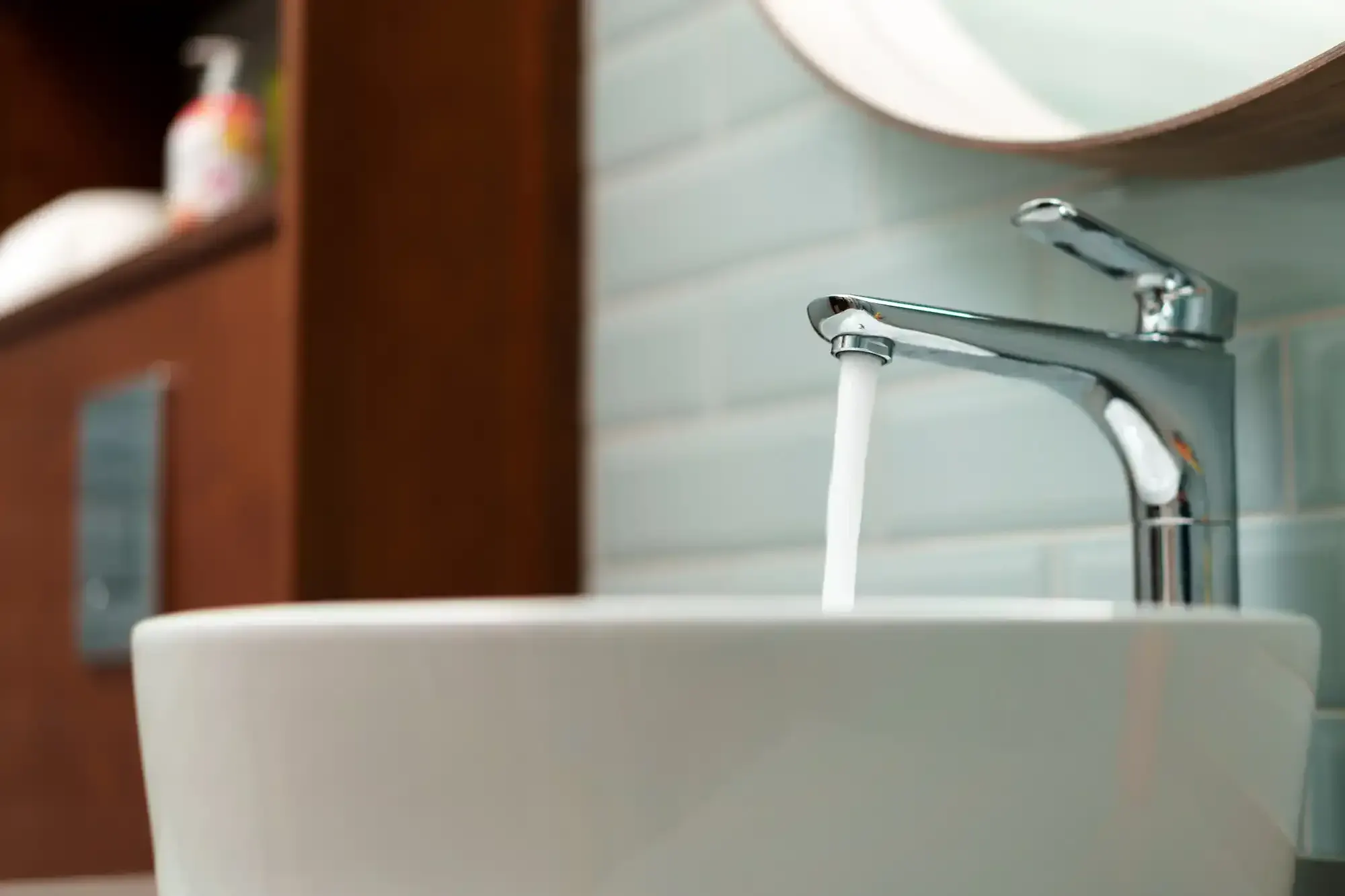 Chrome single-handle faucet running water into a white vessel bathroom sink