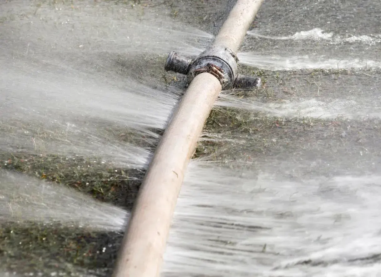 Water spraying from a burst hose coupling lying on grass
