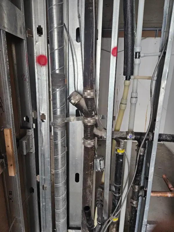 Cast iron waste stack with copper and PEX water lines roughed in behind metal stud framing