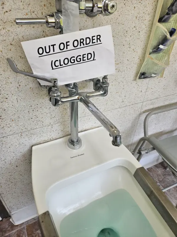 Clogged commercial service sink taped with an "Out of Order" sign before drain cleaning