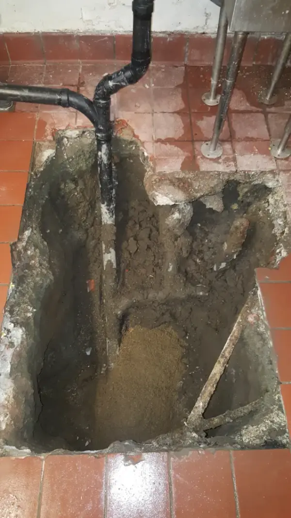Excavation opened through a commercial kitchen tile floor exposing a new ABS drain line