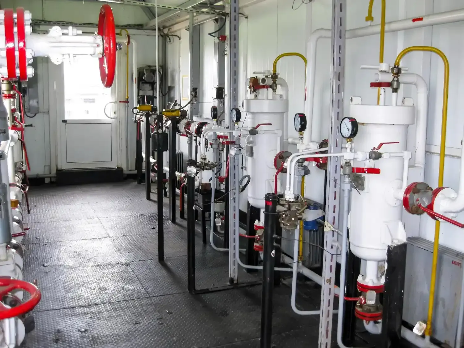 Commercial utility room with white filter tanks, pressure gauges, red valve handwheels and yellow gas lines