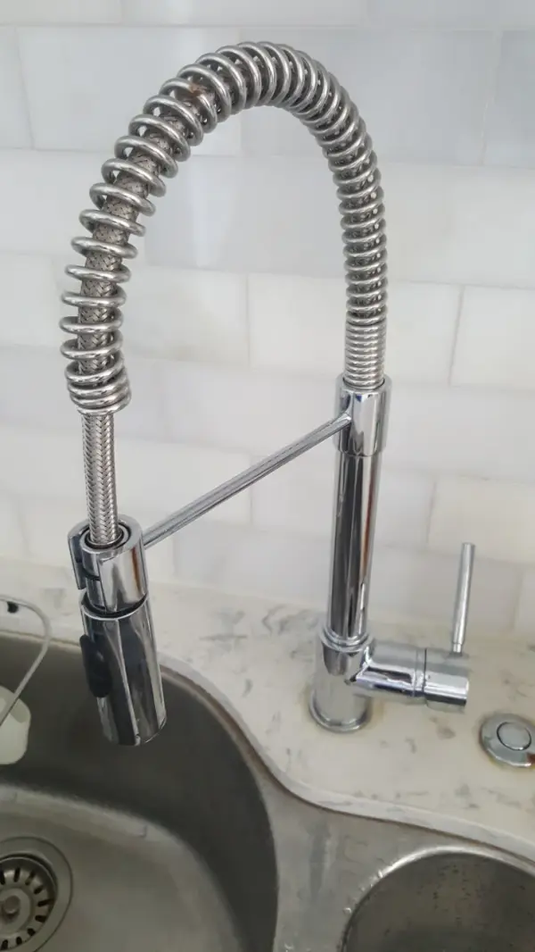 Chrome commercial-style spring kitchen faucet installed on a quartz counter over a double stainless sink