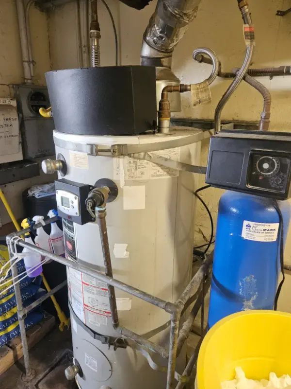 Commercial water heater with a digital control and vent hood next to a blue water softener tank