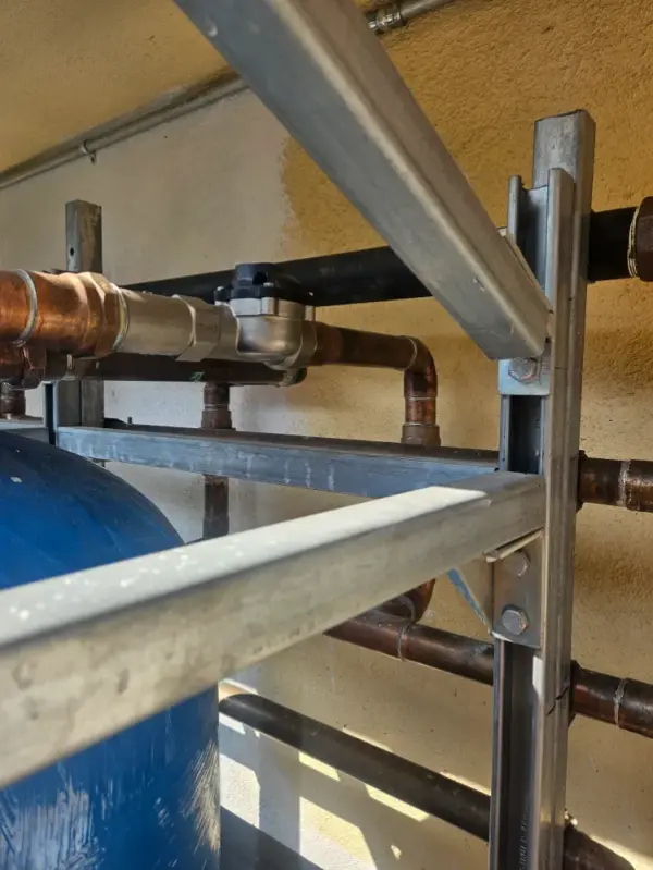 Copper piping and valves racked on strut above a blue water-treatment tank