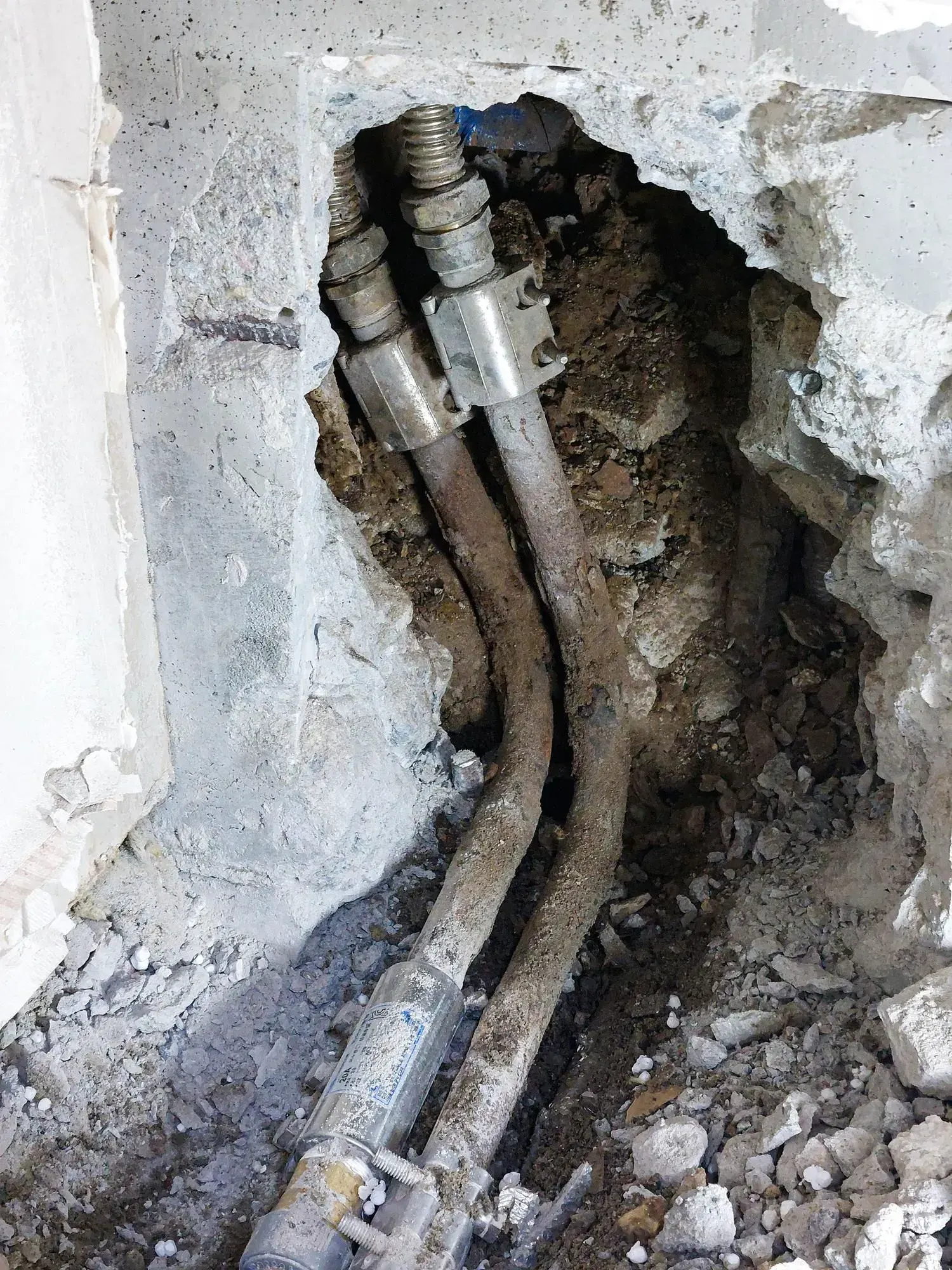 Corroded water supply pipes exposed in a hole broken through a concrete wall