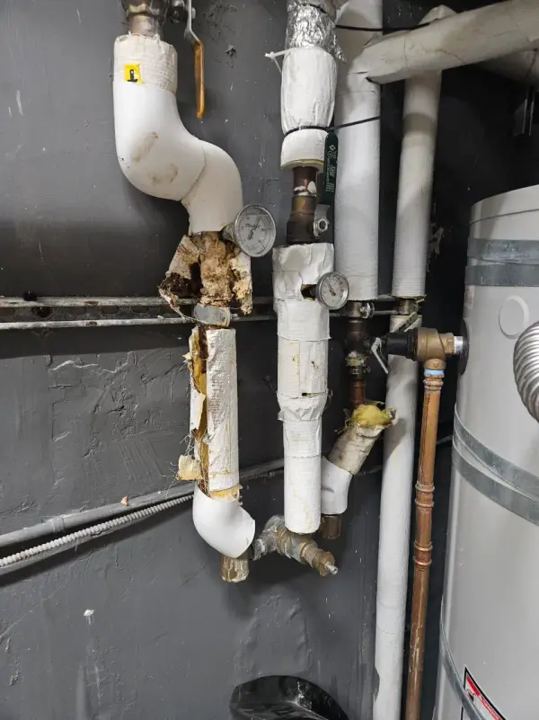 Deteriorated pipe insulation and corroded fittings on the hot water lines beside a storage water heater