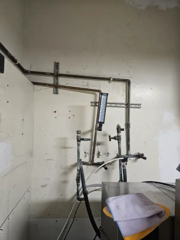 Copper hot and cold water lines with a thermometer and valves dropping to hoses in a commercial dish room
