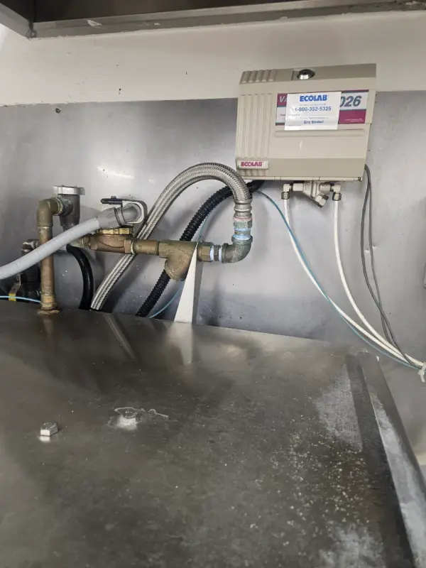 Ecolab dispenser, backflow-protected fill line and hoses above a commercial dish sink
