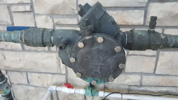 Febco reduced-pressure backflow preventer mounted on copper piping against a stone wall