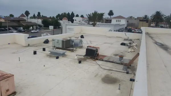 Flat rooftop with HVAC equipment and vents in a residential neighborhood under an overcast sky