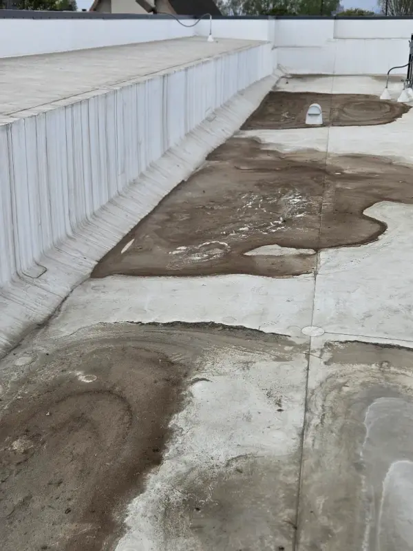 Ponding water and silt across a flat commercial roof between two roof drains