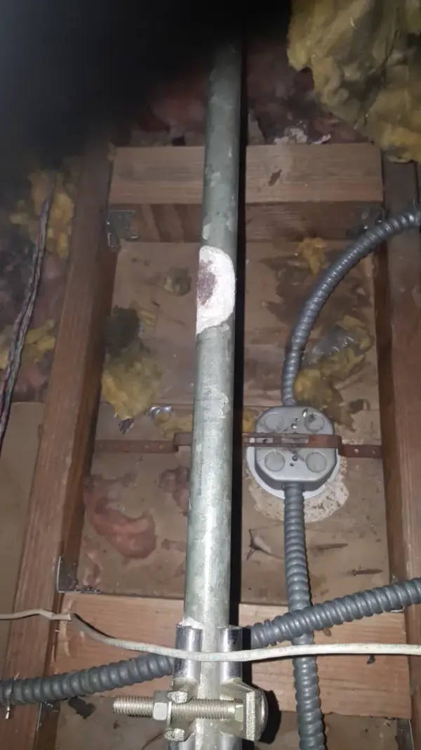Galvanized water line running between floor joists in a crawl space alongside armored electrical cable
