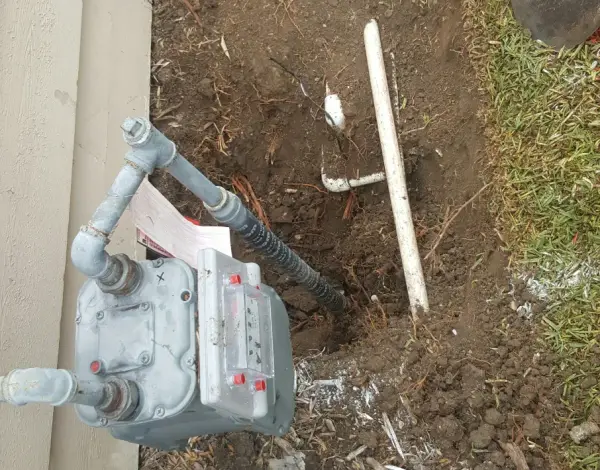 Residential gas meter beside a house wall with a freshly dug trench and new gas line ready to connect
