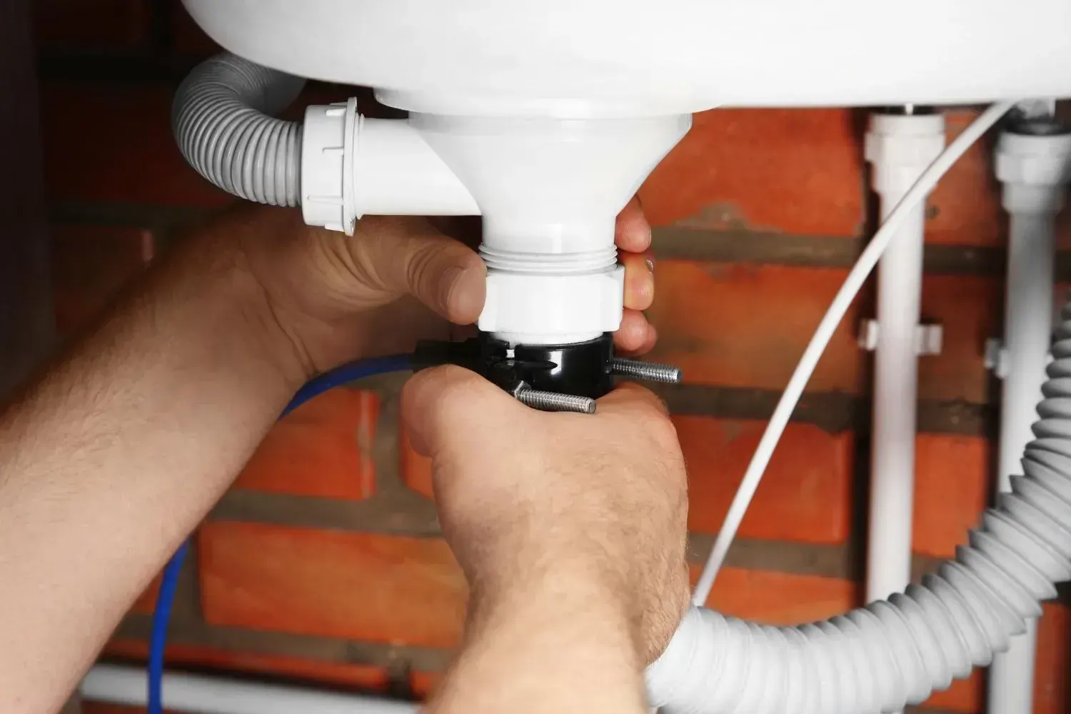 Hands fitting a white plastic drain tailpiece and flexible drain hose under a sink