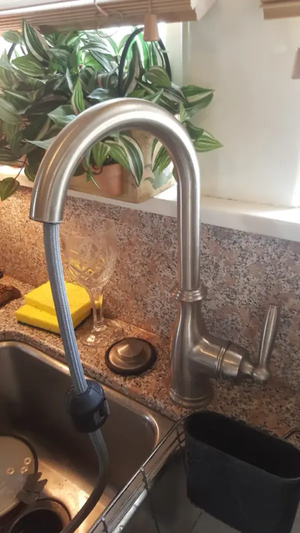 Newly installed brushed-nickel pull-down kitchen faucet on a granite counter beside a stainless steel sink