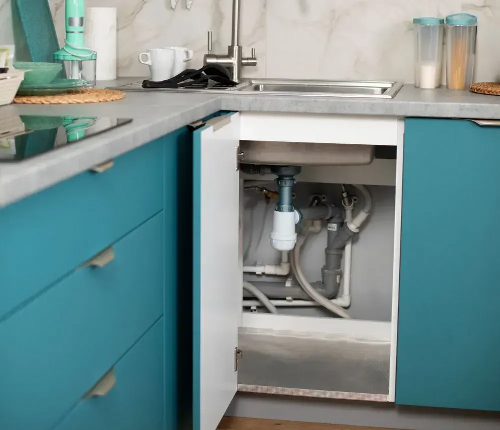 Open kitchen sink cabinet showing the drain trap and water supply lines