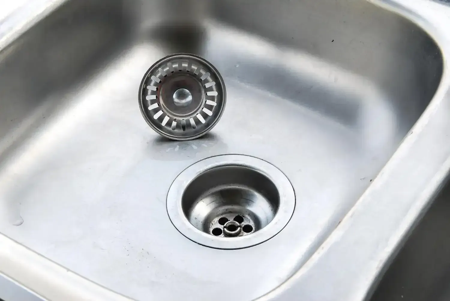 Stainless steel kitchen sink with the basket strainer removed from the drain opening