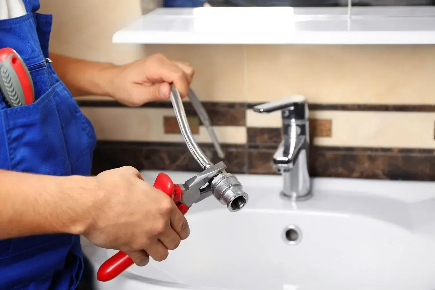 Plumber using pliers to attach a braided supply hose fitting at a bathroom sink