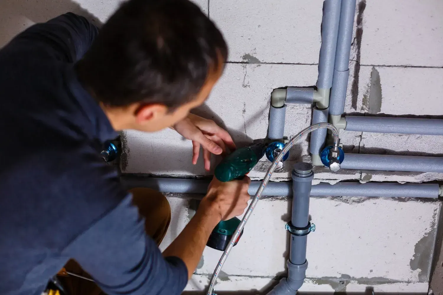 Plumber using a cordless drill to install shutoff valves on insulated wall water pipes