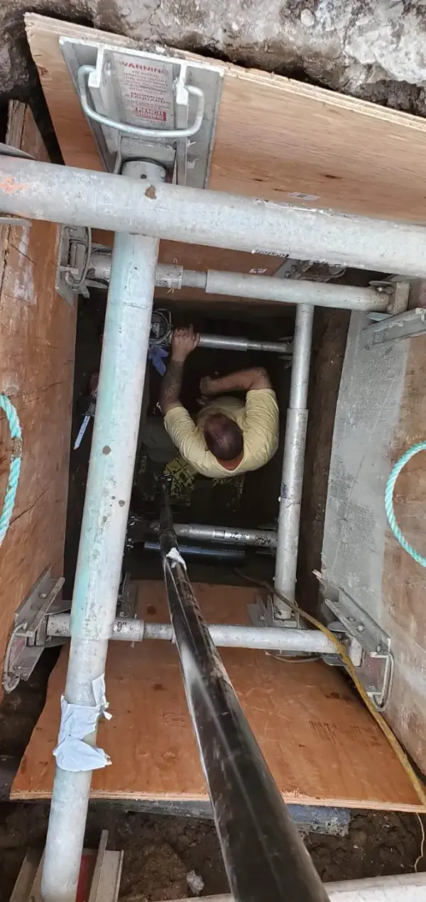 Plumber working at the bottom of a shored access pit as new black HDPE sewer pipe is fed in