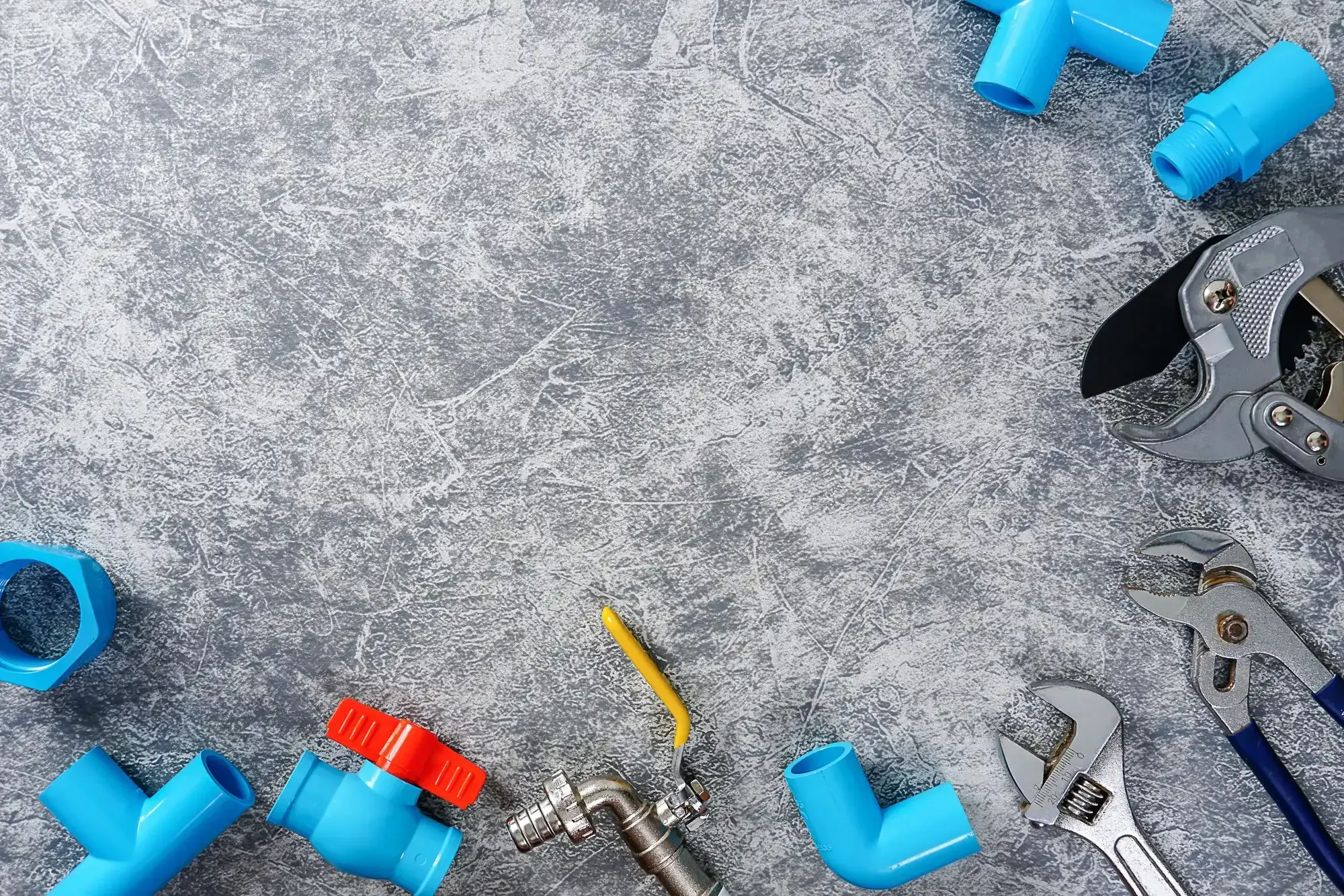 Plumbing fittings, valves and wrenches arranged around a grey work surface