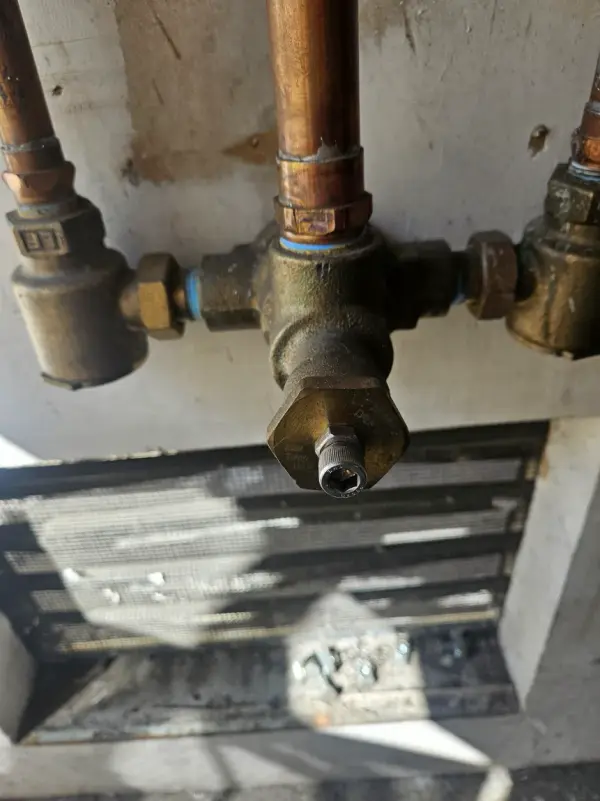 Brass pressure-reducing valve and shutoffs on a copper water manifold above a wall grille