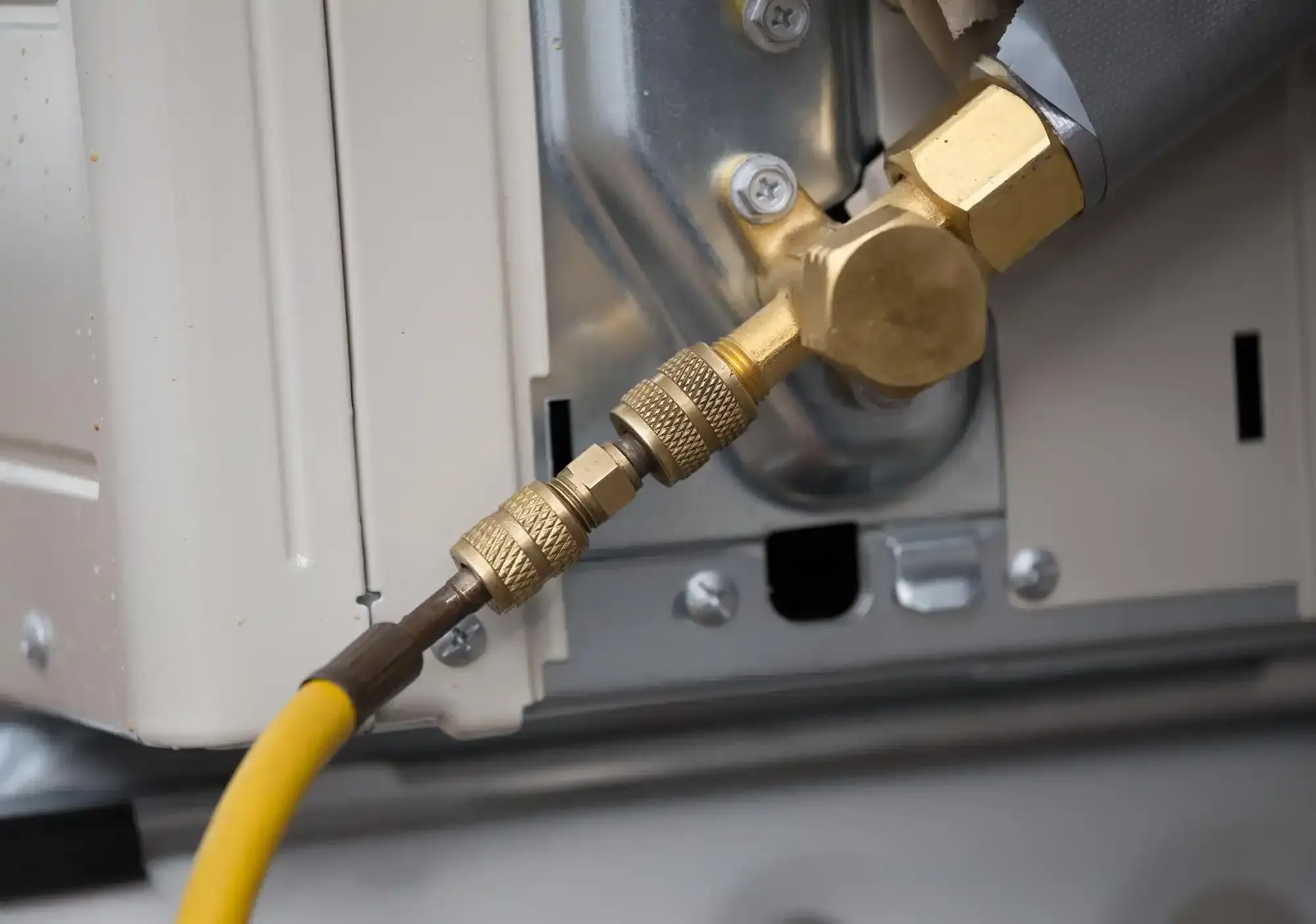 Yellow charging hose attached by brass knurled fittings to the service valve of an outdoor unit