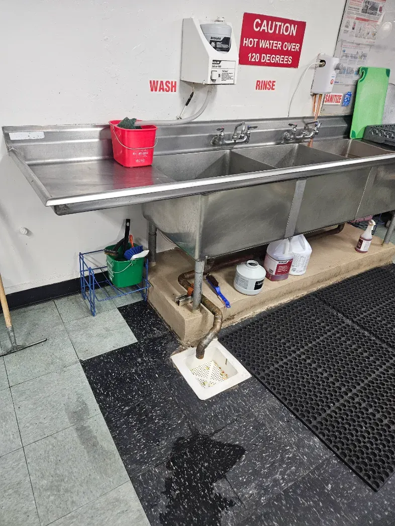 Three-compartment commercial sink draining to a floor sink in a restaurant kitchen