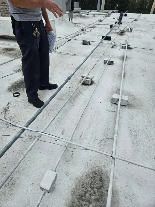 Plumber surveying condensate and gas lines routed on blocks across a commercial roof