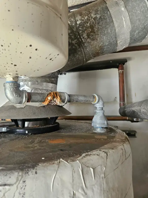 Rusted flue connection and gas line on top of an aging commercial water heater