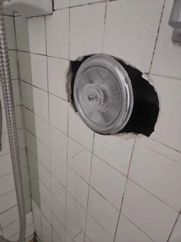 Shower valve with a clear plastic cover in an opening cut through white wall tile during replacement