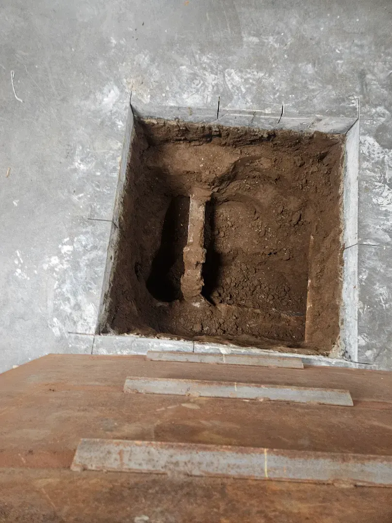 Square opening cut through a concrete slab exposing the rusted pipe run below