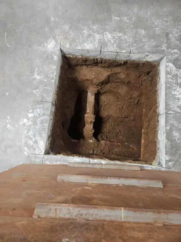 Square opening cut through a concrete slab exposing the rusted pipe run below