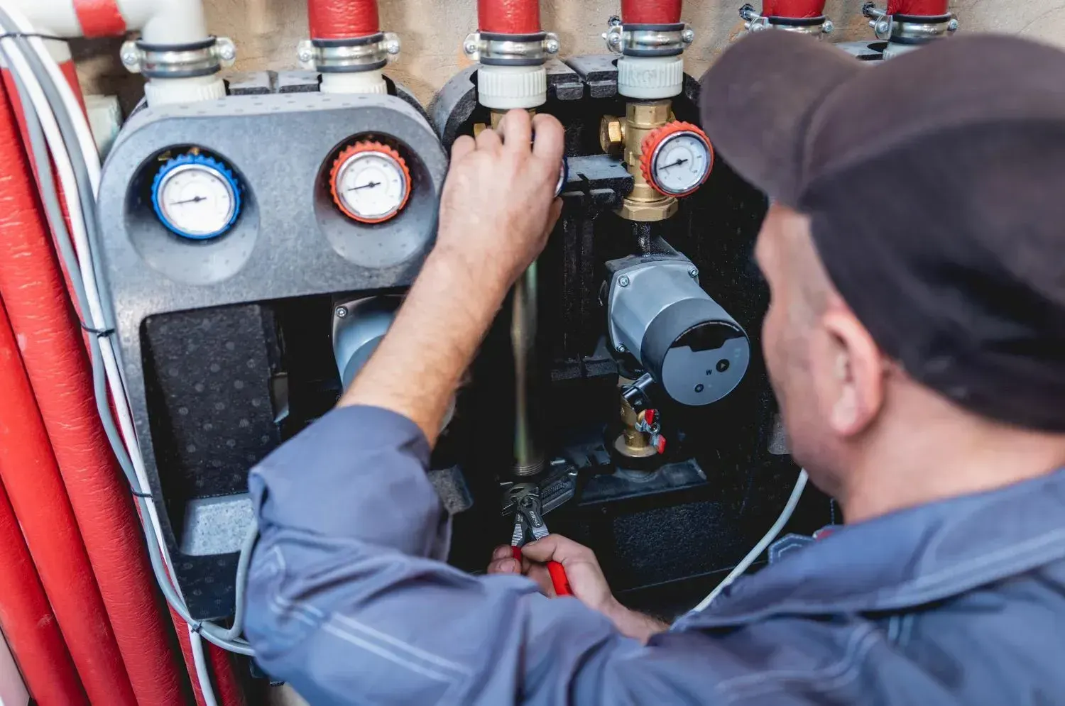 Technician adjusting a hydronic pump station with pressure gauges and red insulated pipes
