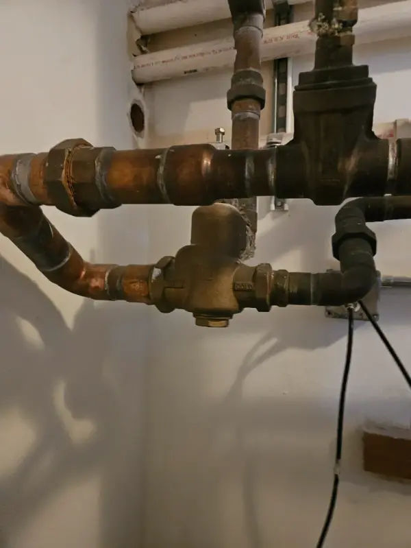 Brass thermostatic mixing valve piped between the hot and cold copper lines at a water heater
