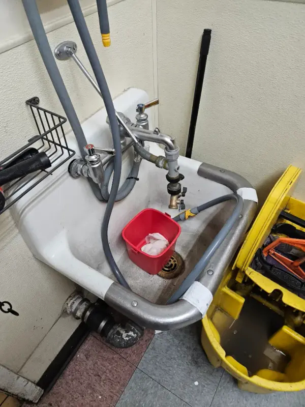 Wall-hung service sink with a hose bibb and vacuum breaker beside a mop bucket