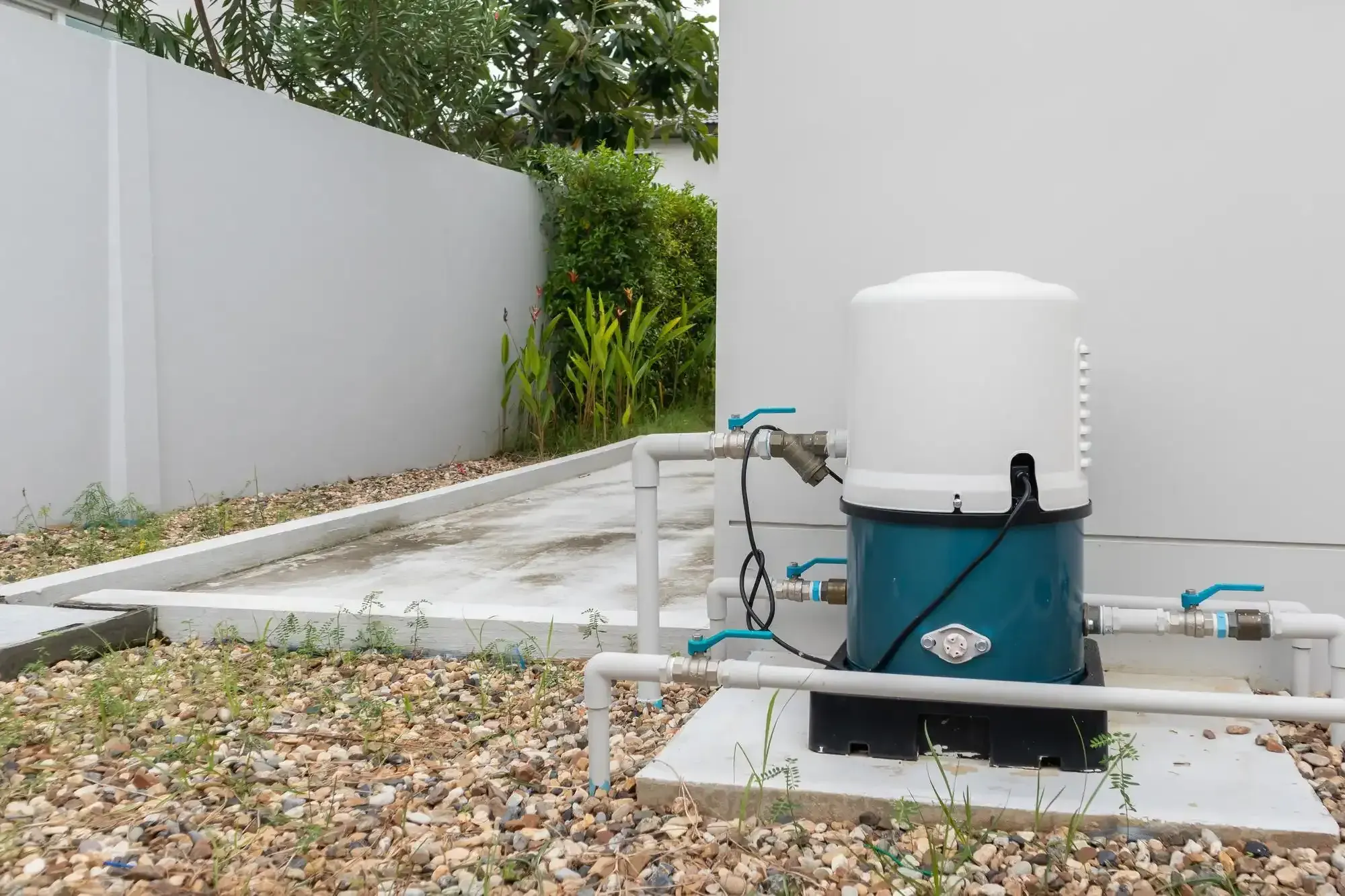 Outdoor residential water booster pump with white PVC pipes and blue ball valves