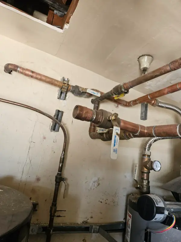 Copper water piping, a Watts ball valve and a pressure gauge in a mechanical closet above a water heater