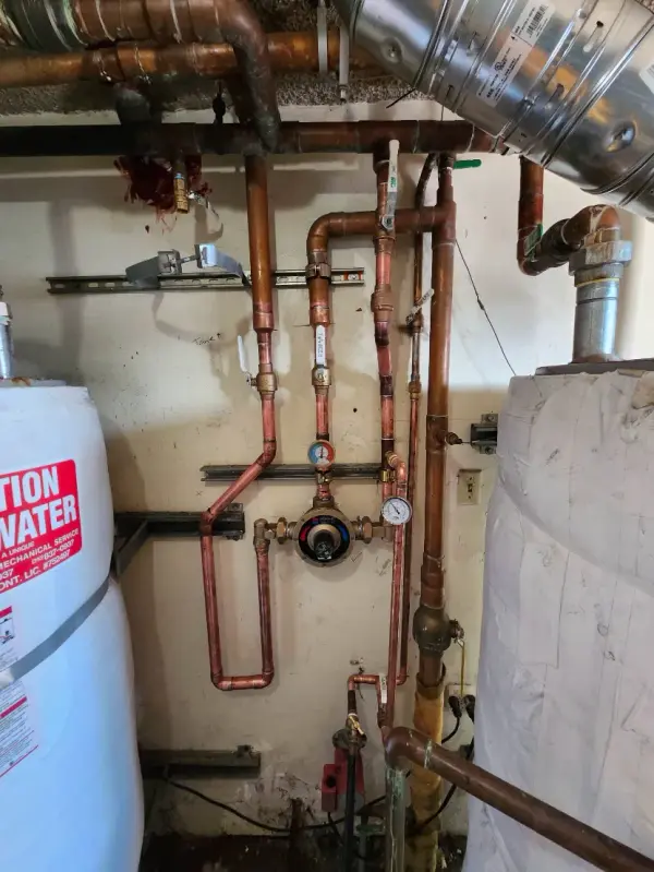 Basement utility room with copper pipes, valves, water heater, and ductwork along the wall