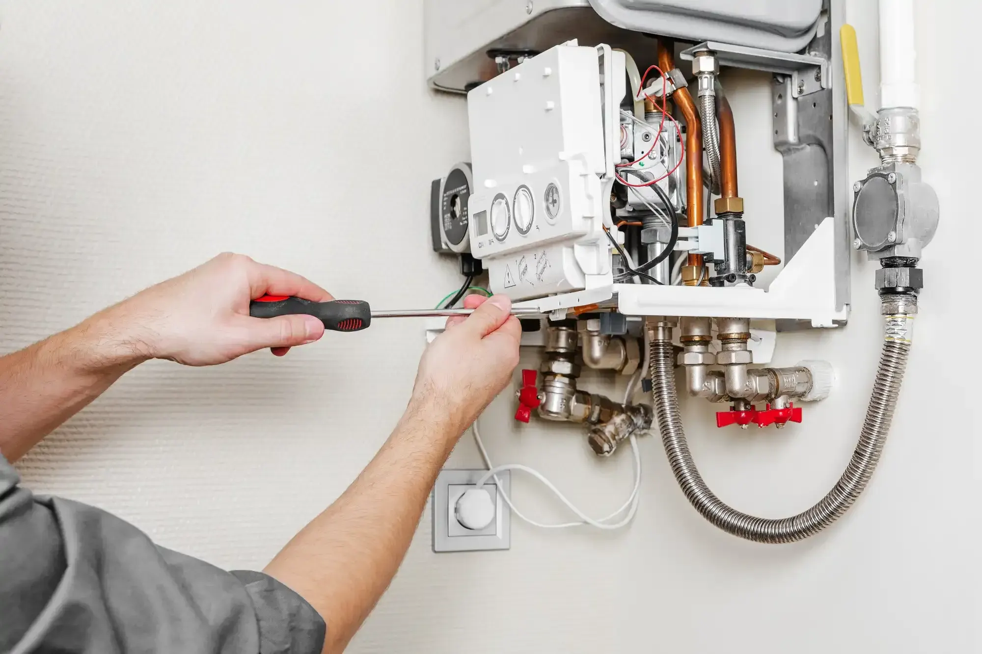 Technician using a screwdriver on the opened control panel of a wall-mounted gas water heater