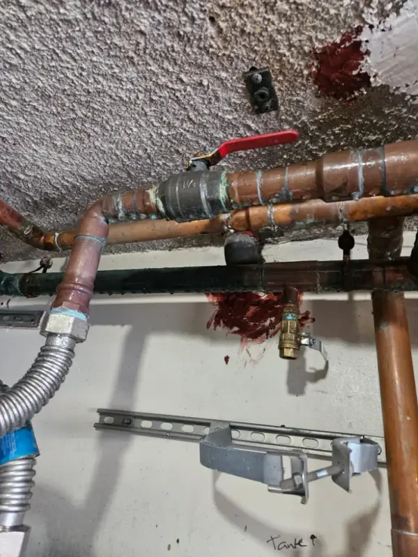 Copper and steel water lines with a ball valve below a ceiling, marked for a water heater tie-in