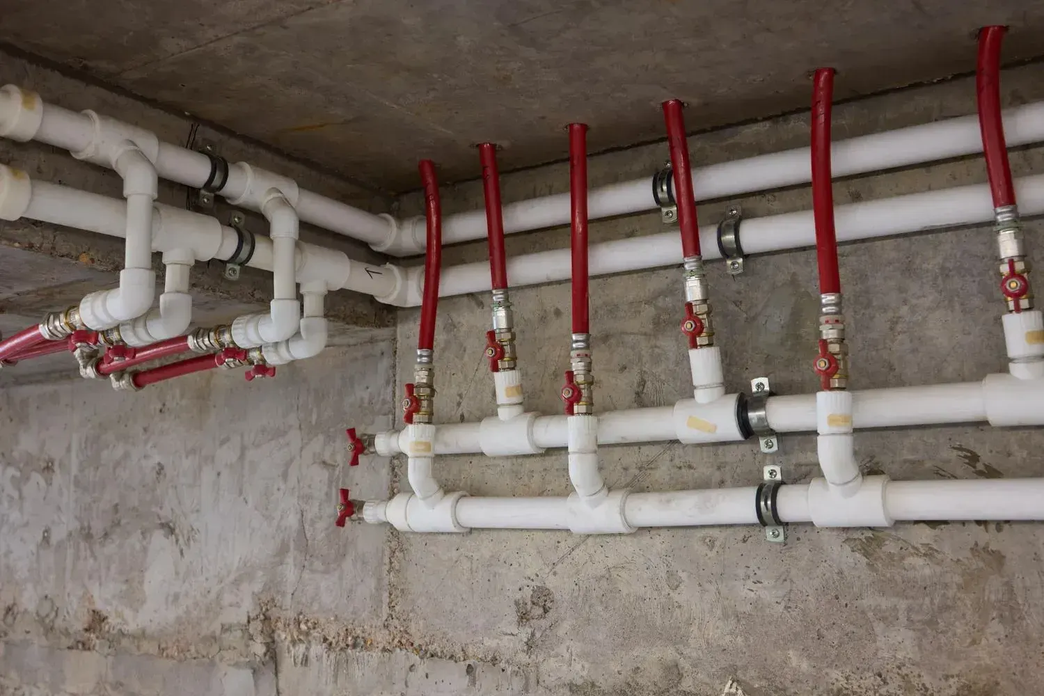 White PPR water supply pipes with red-handled valves and red lines mounted on a concrete wall