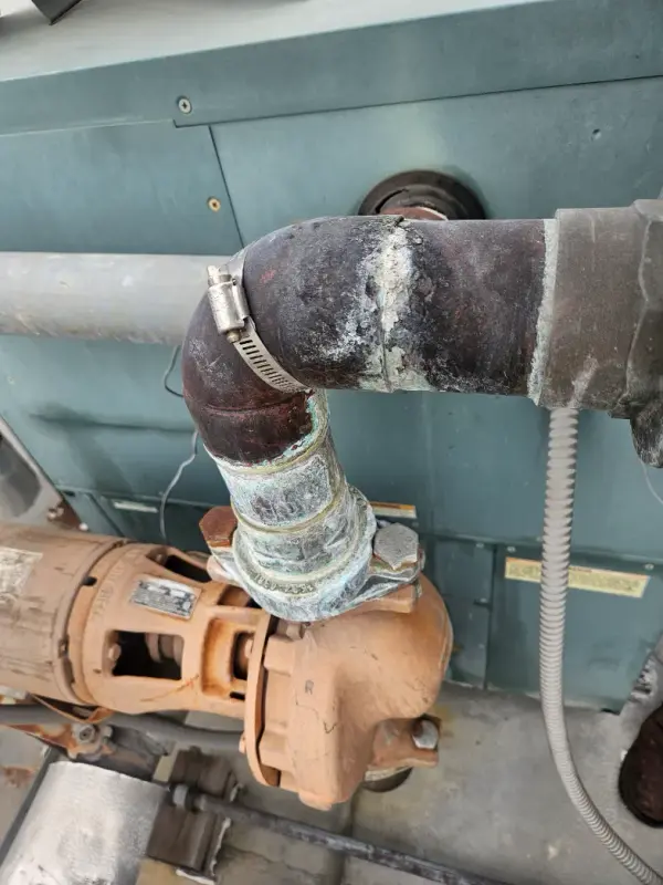 Worn copper discharge elbow clamped to a pump on a commercial mechanical unit